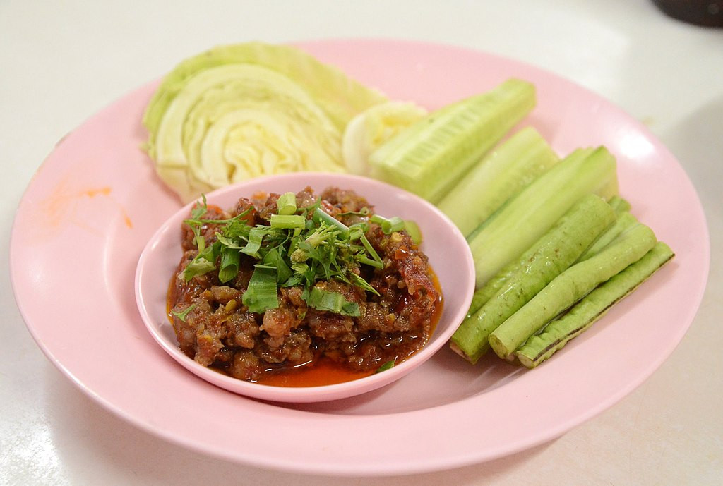 picture of Nam Phrik, served with a slice of fresh cabbage, green beans, and cucumbers.